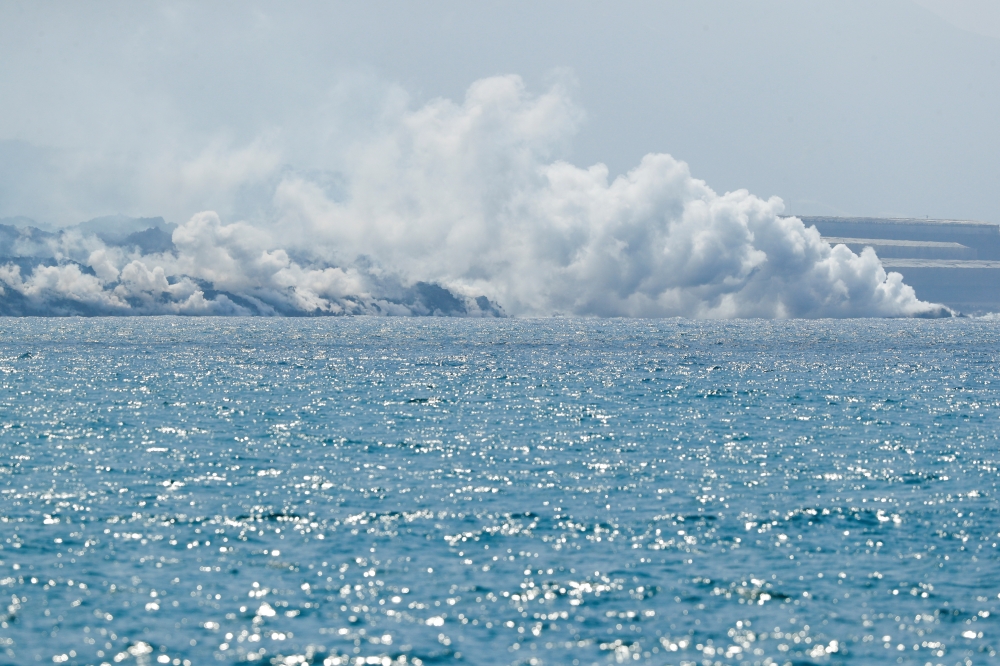 Lava flows and smoke rises, as seen from Tazacorte Port, following the eruption of a volcano on the Canary Island of La Palma, Spain, September 30, 2021. REUTERS/Borja Suarez