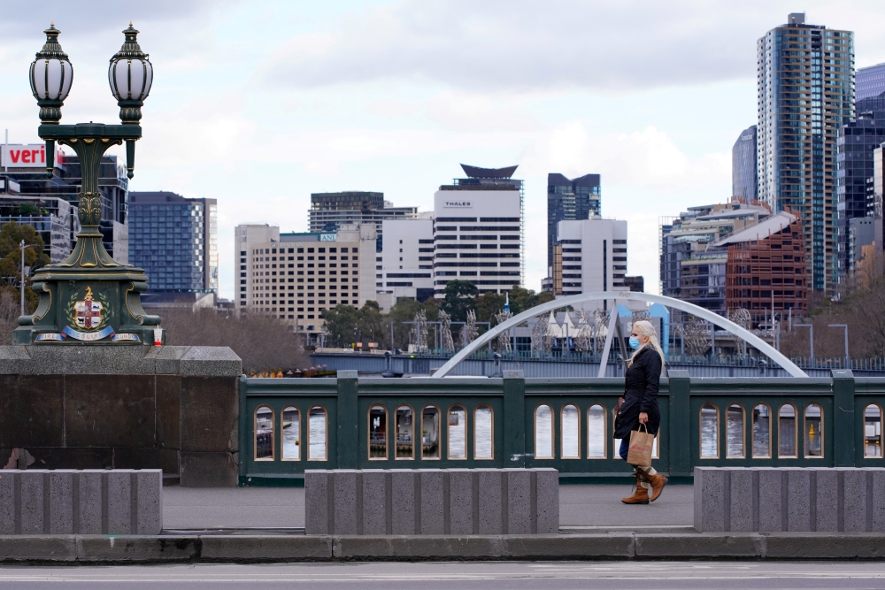 A lone woman, wearing a protective face mask, walks across a city centre bridge as the state of Victoria looks to curb the spread of a coronavirus disease (COVID-19) outbreak in Melbourne, Australia, July 16, 2021. REUTERS/Sandra Sanders/File Photo