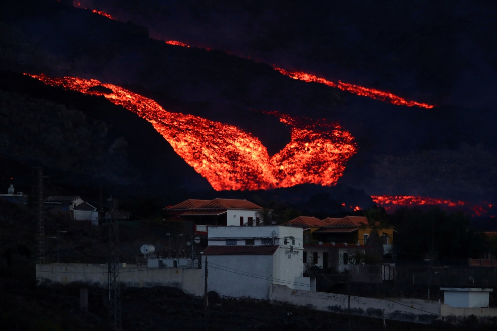Lava flows down behind houses in Los Llanos as the Cumbre Vieja volcano continues to erupt on the Canary Island of La Palma, as seen from Tajuya, Spain, October 13, 2021. REUTERS/Sergio Perez