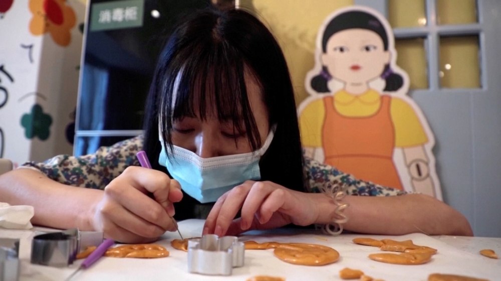 A customer uses a tool to cut a biscuit into a shape during a session of a South Korean Netflix show Squid Game-themed confection-making event, at a bakery in Beijing, China in this screengrab from a video taken on October 16, 2021. REUTERS TV via REUTERS