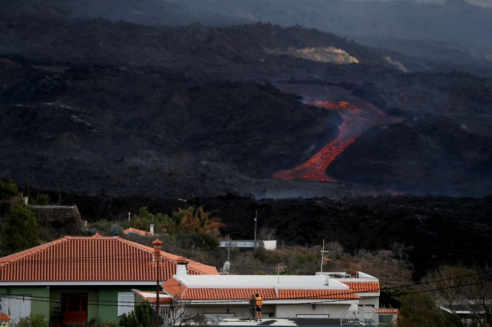 Two people look at lava spewed from the Cumbre Vieja volcano from a house nearby as it continues to erupt on the Canary Island of La Palma, as seen from Tajuya, Spain, October 20, 2021. Reuters/Susana Vera