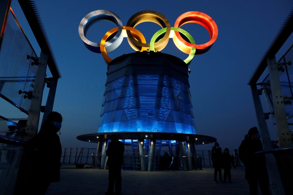 People wearing face masks following the coronavirus disease (COVID-19) outbreak are seen near the lit-up Olympic rings at top of the Olympic Tower, a year ahead of the opening of the 2022 Winter Olympic Games, in Beijing, China February 4, 2021. REUTERS/T
