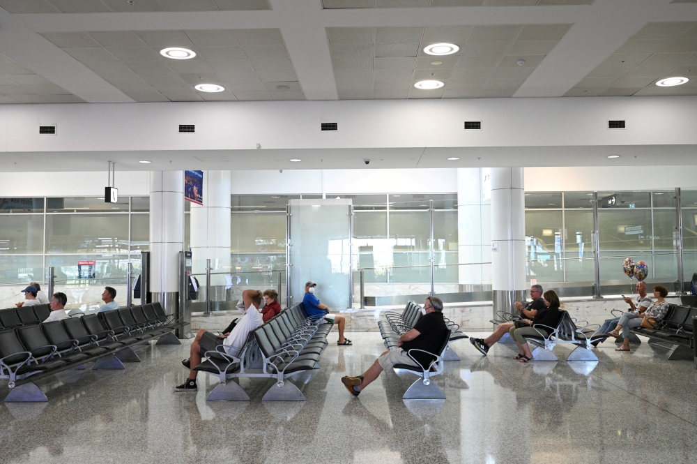 People sit in the arrivals section of the international terminal of Kingsford Smith International Airport the morning after Australia implemented an entry ban on non-citizens and non-residents intended to curb the spread of the coronavirus disease (COVID-19) in Sydney, Australia, March 21, 2020. REUTERS/Loren Elliott/File Photo