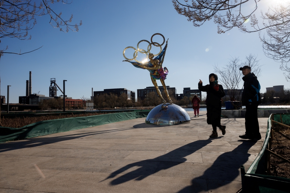People stand next to a statue featuring the Olympic Rings outside the headquarters of the Beijing Organising Committee for the 2022 Olympic and Paralympic Winter Games in Shougang Park, the site of a a former steel mill, in Beijing, China, November 30, 2021. REUTERS/Thomas Peter/File Photo