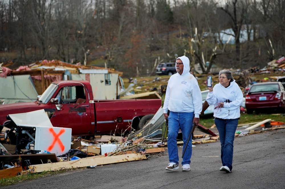 Bill Mosley walks with his wife Bonnie while carrying two of his guns, the only items he was able to recover after their home was destroyed, as a devastating outbreak of tornadoes ripped through several U.S. states in Earlington, Kentucky, U.S. December 11, 2021. REUTERS/Cheney Orr