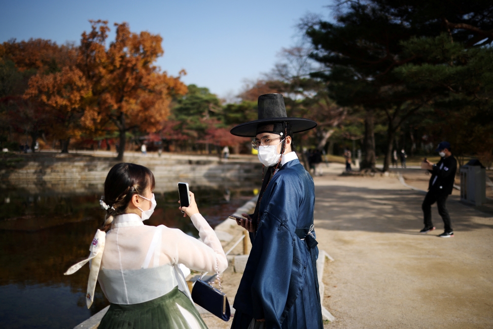 A couple dressed in Korea's traditional Hanbok costume, wearing protective face masks to avoid contracting the coronavirus, enjoy an autumn day at Gyeongbok palace in Seoul, South Korea, November 17, 2021. REUTERS/Kim Hong-Ji/File Photo