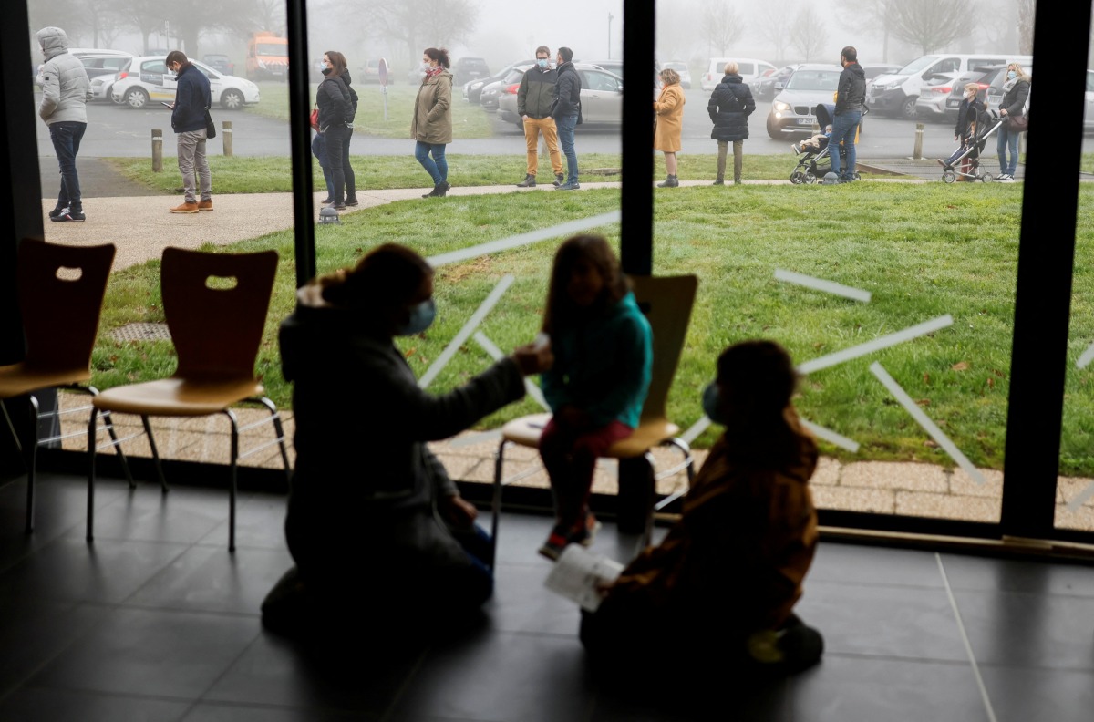 A mother administers a COVID-19 saliva test to her child as people stand in a queue at a coronavirus disease (COVID-19) testing centre in Saint-Hilaire-de-Loulay near Nantes, France, January 17, 2022. REUTERS/Stephane Mahe
