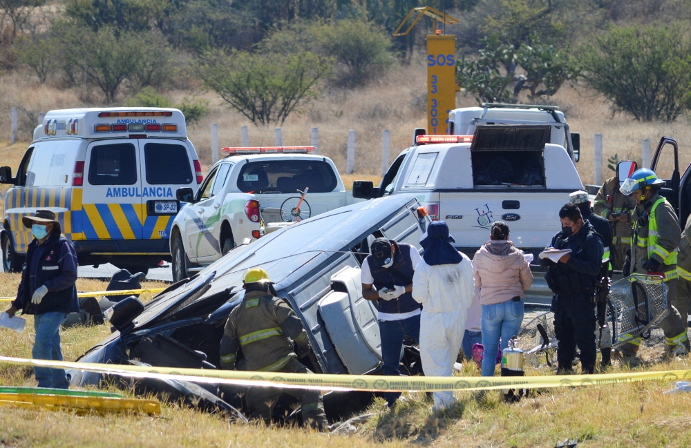 An emergency crew members, including a forensic worker and a firefighter, work next to a damaged vehicle at the site of an accident after a van overturned and flipped into a ditch on a highway in central Mexico, near the city of Lagos de Moreno, Mexico January 29, 2022. REUTERS/Liberto Urena