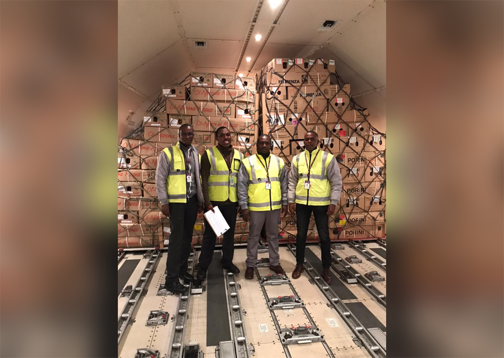 Qatar Airways Cargo employees pose with boxes full of roses behind them.