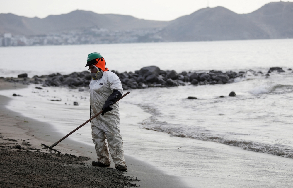 A worker cleans up an oil spill at the beach as demonstrators take part in a protest outside Repsol's La Pampilla refinery against the recent oil spill that has caused an ecological disaster on the coast of Lima, in Ventanilla, Peru January 29, 2022. REUTERS/Angela Ponce/File Photo