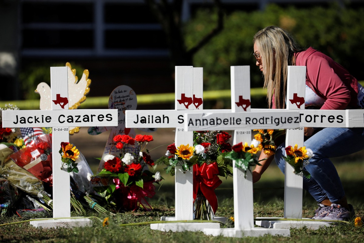 A woman lays a flower next to crosses with the names of victims of a school shooting, at a memorial outside Robb Elementary school, two days after a gunman killed nineteen children and two adults, in Uvalde, Texas, U.S. May 26, 2022. REUTERS/Marco Bello
