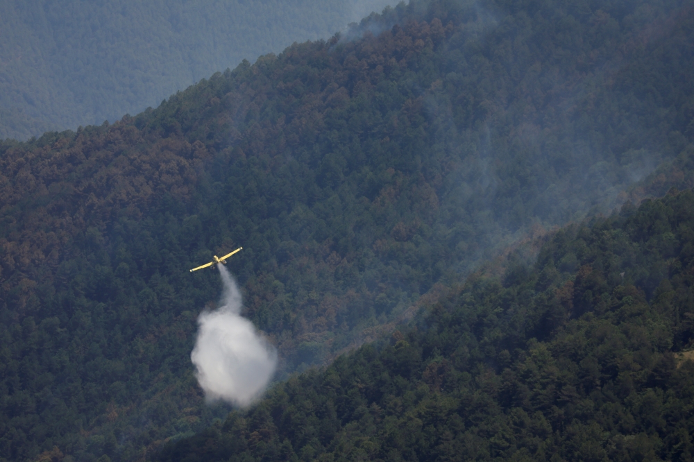 A plane drops water onto a wildfire near Lladurs, Spain, June 17, 2022. REUTERS/Albert Gea
