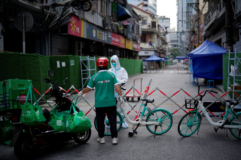 A worker in a protective suit gets food from a delivery worker at a closed residential area during lock-down, amid the coronavirus disease (COVID-19) outbreak, in Shanghai, China, on May 25, 2022. (REU-TERS/Aly Song/File Photo)