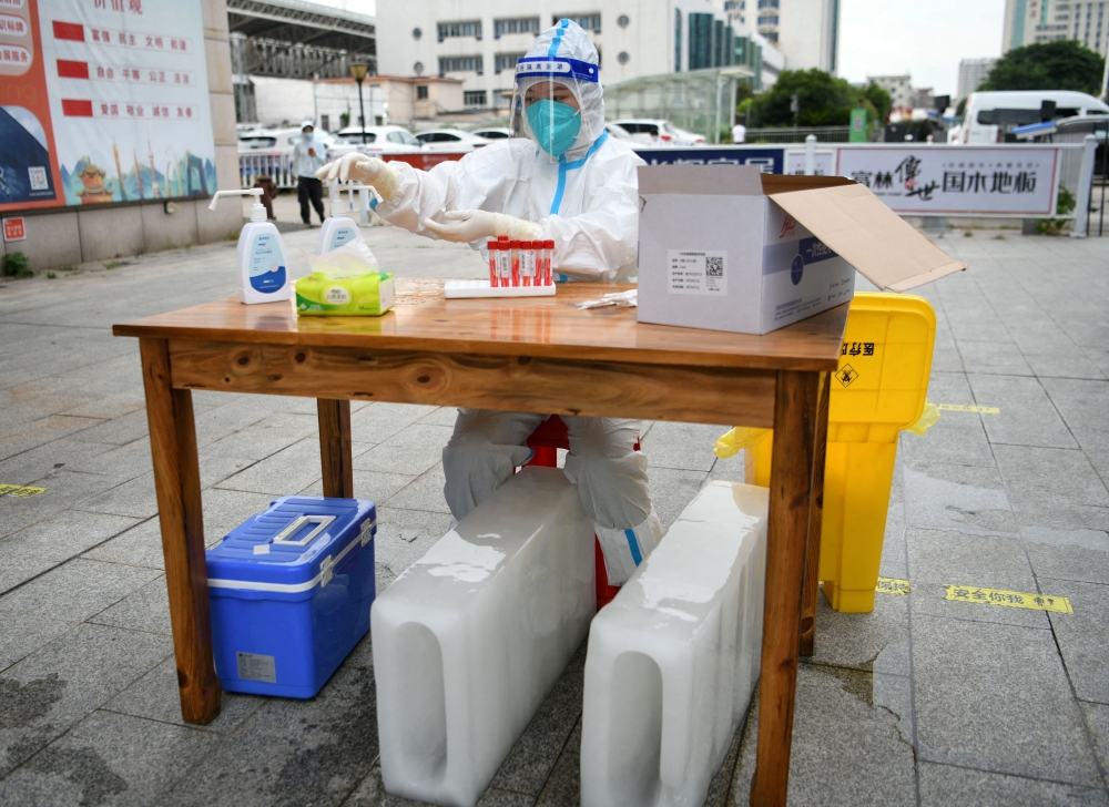 A medical worker in a protective suit sits with ice blocks at a nucleic acid testing site during preparations to test residents for the coronavirus disease (COVID-19), amid a heatwave warning in Nanchang, Jiangxi province, China July 21, 2022. China Daily via REUTERS 