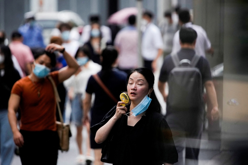 A woman wearing face mask uses a fan as she walks on a street on a hot day, following the coronavirus disease (COVID-19) outbreak in Shanghai, China July 19, 2022. REUTERS/Aly Song/File Photo/File Photo