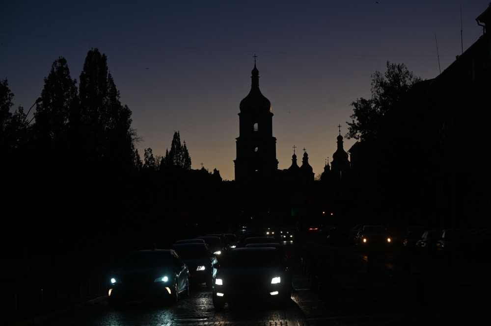 Vehicles drive along a street with the St. Sophia Cathedral silhouetted in the background, as the city is plunged into near darkness following a military strike that partially brought down the power infrastructure, in Kyiv, on October 31, 2022. (Sergei SUPINSKY / AFP)