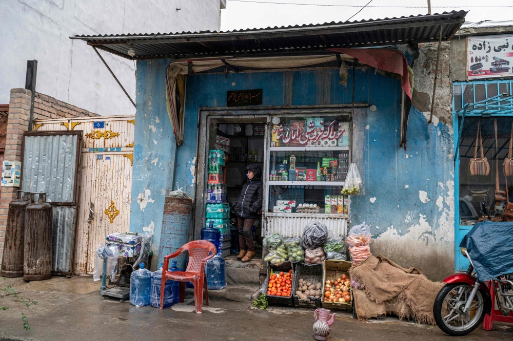 An Afghan boy stands by the door of a shop in Kabul on November 13, 2022. (Photo by Wakil KOHSAR / AFP)