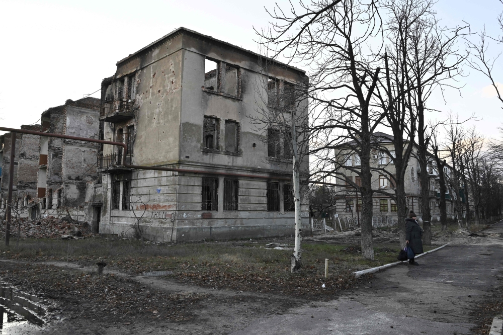 A local resident walks in front of a destroyed residential building in the town of Lyman, Donetsk region, on December 14, 2022, amid the Russian invasion of Ukraine. (Photo by Genya SAVILOV / AFP)