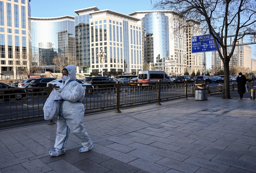 A woman wearing personal protective equipment (PPE) amid the Covid-19 pandemic walks along a street in Beijing on December 26, 2022. (Photo by Noel CELIS / AFP)