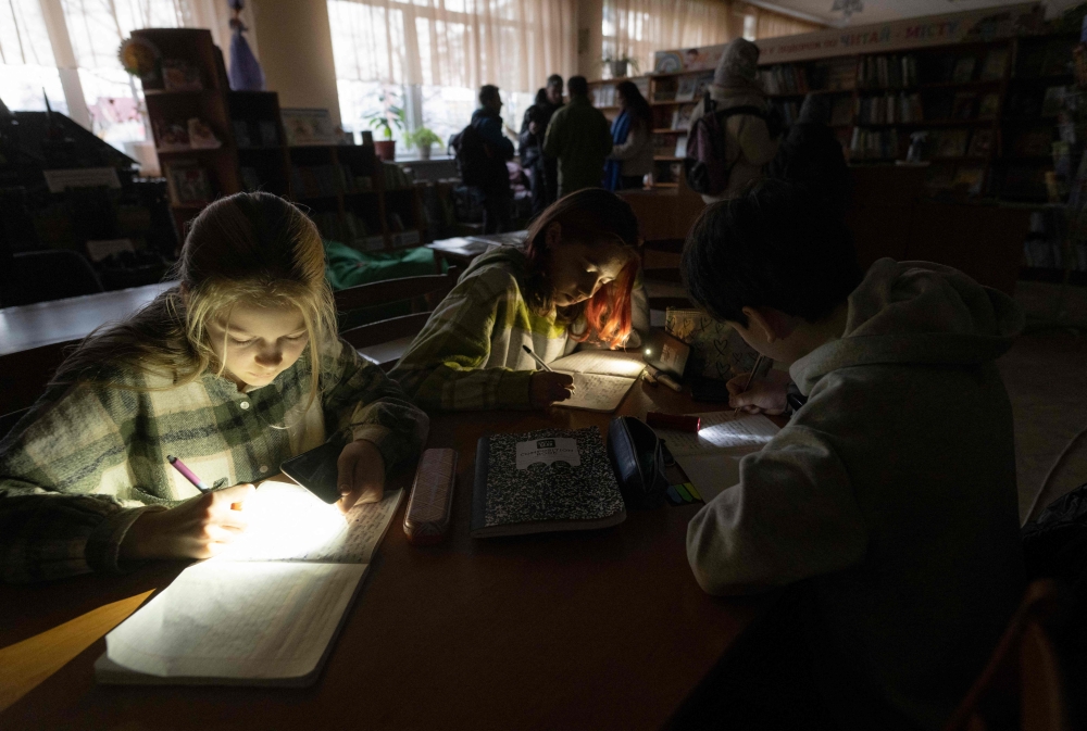 Children use flashlights as they attend a meeting of their literature club in a public library during a power outage in Irpin, northwest of Kyiv, on December 23, 2022, amid the Russian invasion of Ukraine. (Photo by Genya SAVILOV / AFP)