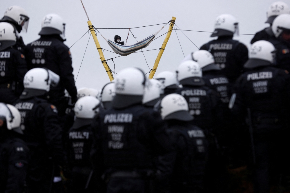 Police officers stand guard as an activist lies in a hammock connected to a structure, as activists demonstrate at Luetzerath, a village that is about to be demolished to allow for the expansion of the Garzweiler open-cast lignite mine of Germany's utility RWE, Germany, January 10, 2023. (REUTERS/Thilo Schmuelgen)