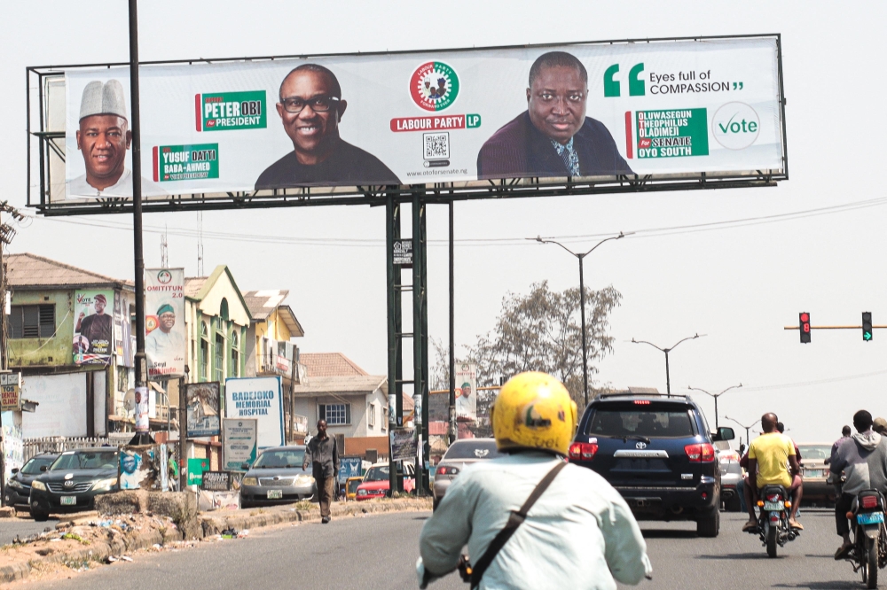 Motorcycle taxi drivers carry passengers as they ride past campaign posters of Peter Obi, presidential candidate of the Labour Party, in Ibadan, south-west of Nigeria on January 17, 2023. (Photo by Samuel Alabi / AFP)