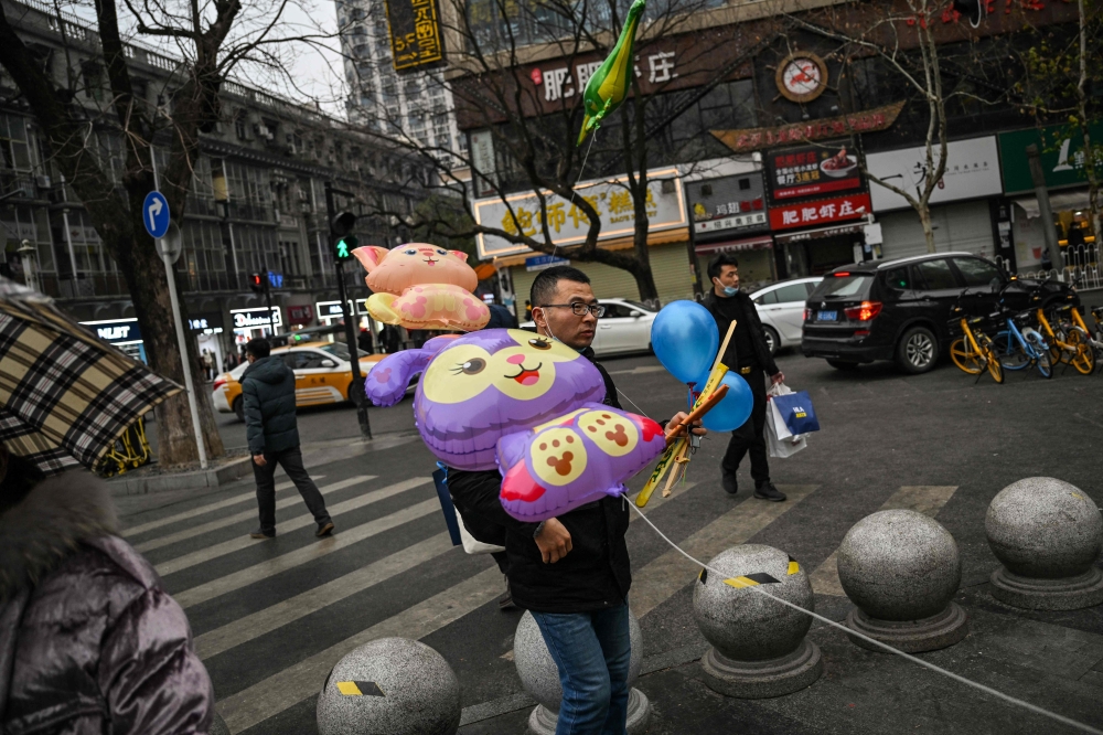People walk on a street in Wuhan, in China's central Hubei province, on January 21, 2023. (Photo by Hector RETAMAL / AFP)