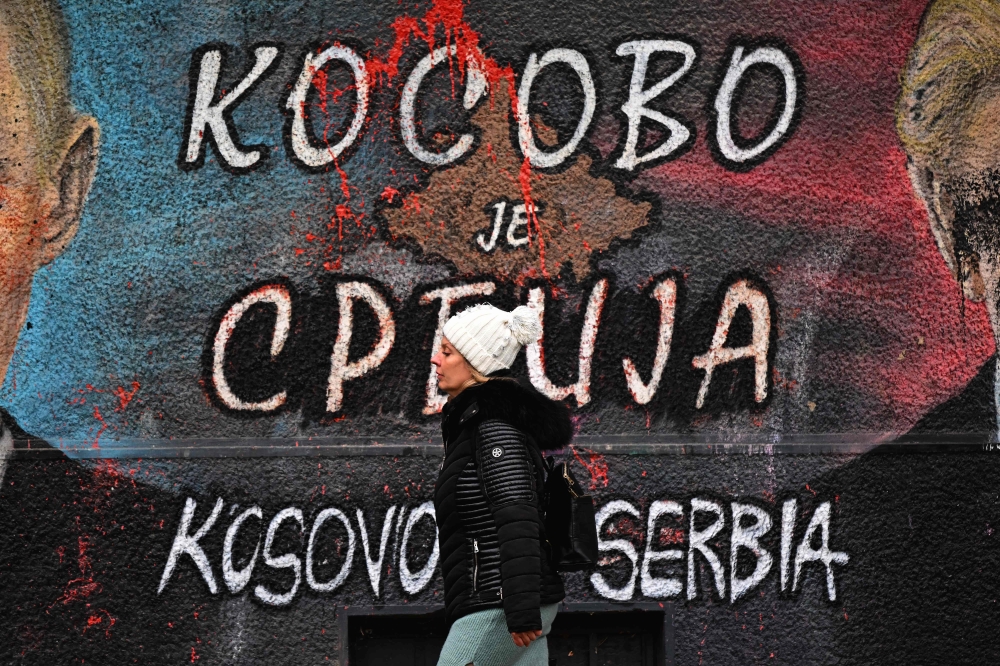 A pedestrian walks past a mural painting depicting the map of Kosovo with both cyrillic and english writing, reading 