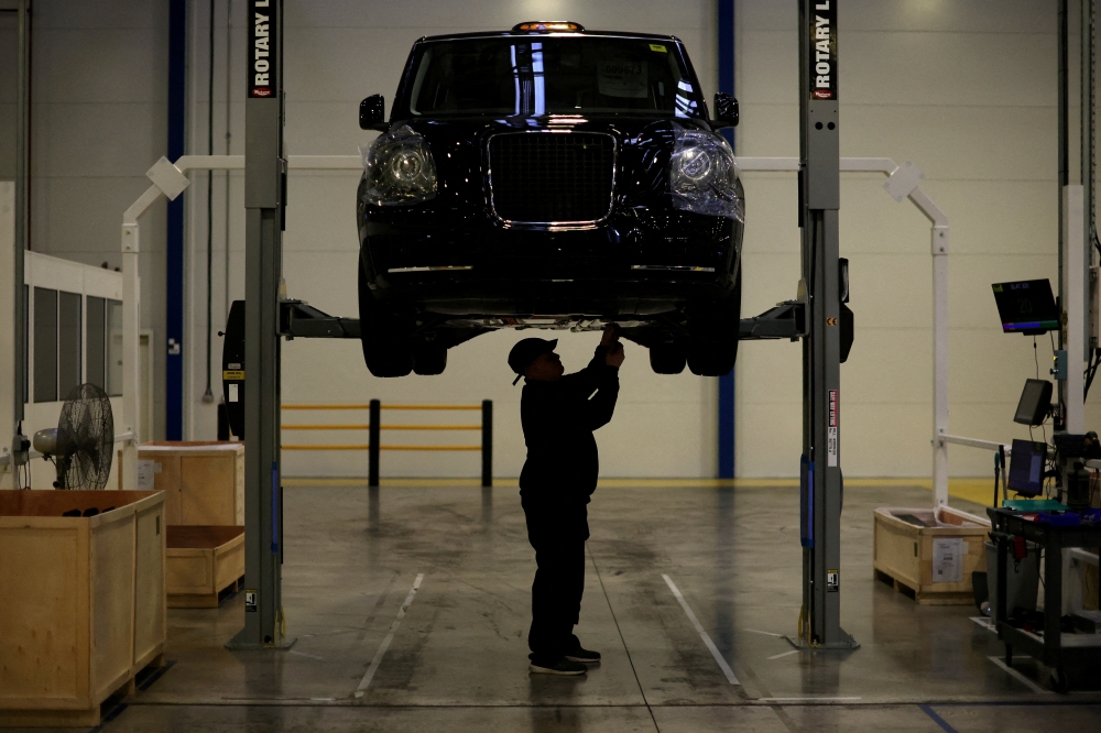 A worker stands beneath a TX electric taxi inside the LEVC (London Electric Vehicle Company) factory in Coventry. File Photo: Phil Noble/Reuters
