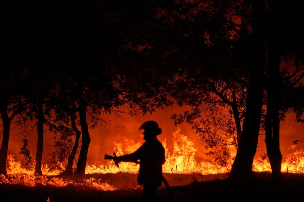 In this file photo taken on September 12, 2022 a firefighter stands in front of flames at a night wildfire in Saumos near Bordeaux, southwestern France. Photo by PHILIPPE LOPEZ / AFP