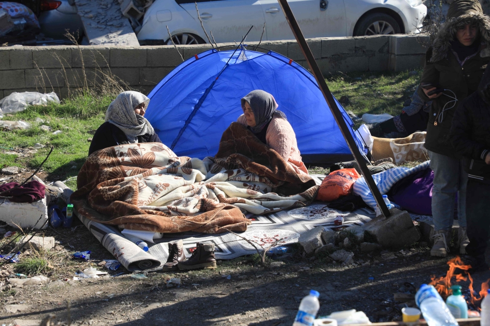 Two women sit next to a tent in Nurdagi, in the countryside of Gaziantep, on February 9, 2023, three days after a deadly earthquake that hit Turkey and Syria. (Photo by Zein Al Rifai / AFP)