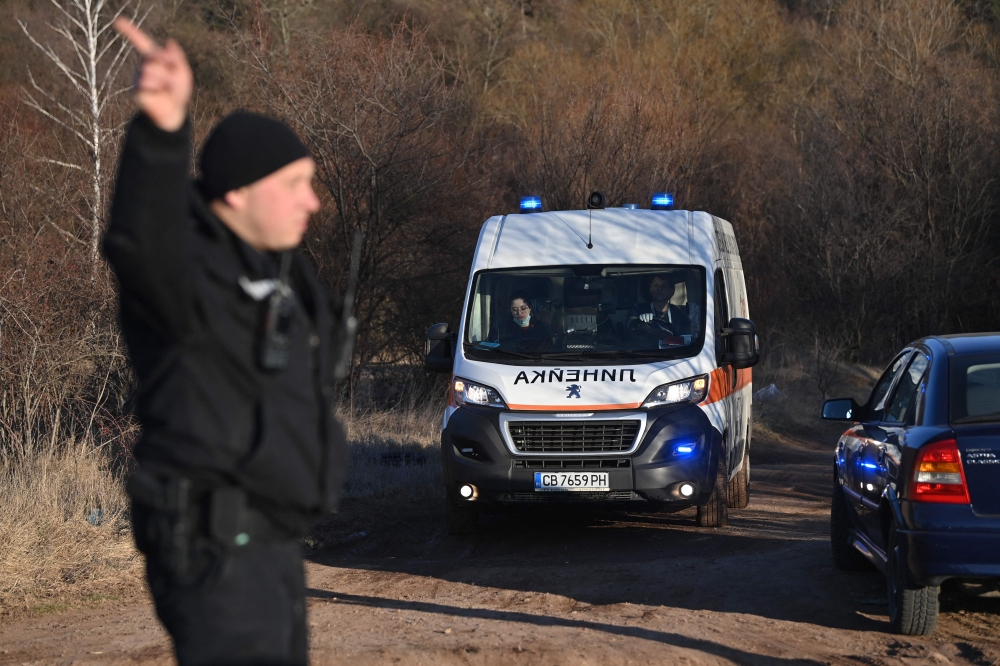A security official gestures as an ambulance moves on the outskirts of the village of Lokorsko, some 20 kilometres (12 miles) north-east of Sofia, after the discovery of eighteen dead migrants in the rear of an abandoned truck. (Photo by NIKOLAY DOYCHINOV / AFP)