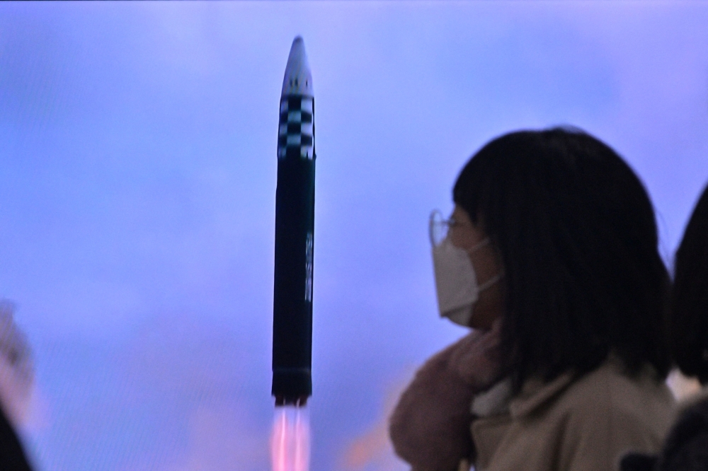 A woman walks past a television showing a news broadcast with file footage of a North Korean missile test, at a railway station in Seoul on February 18, 2023. (Photo by Anthony Wallace / AFP)