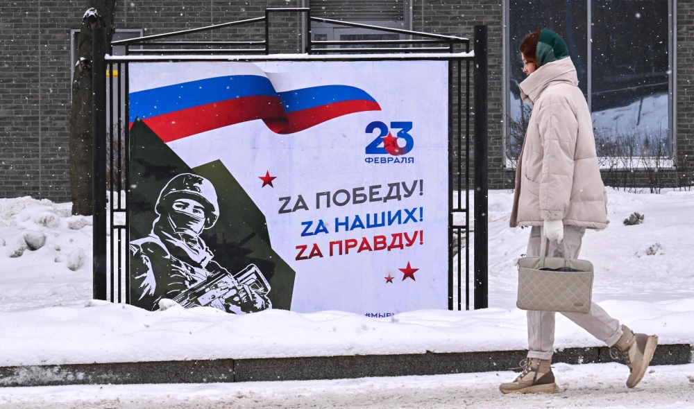 A woman walks past a poster dedicated to the upcoming Defender of the Fatherland Day which depicts a service member and reads 