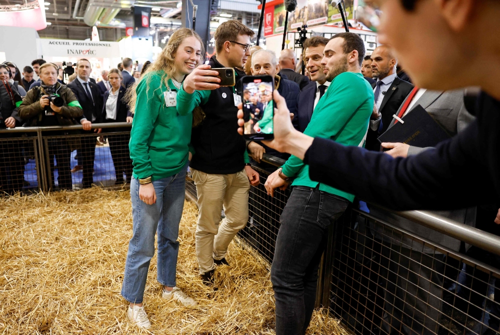 French President Emmanuel Macron poses with visitors for photograph as he visits the 59th edition of the International Agriculture Fair on its inauguration day in Paris, on February 25, 2023. (Photo by CHRISTIAN HARTMANN / POOL / AFP)
