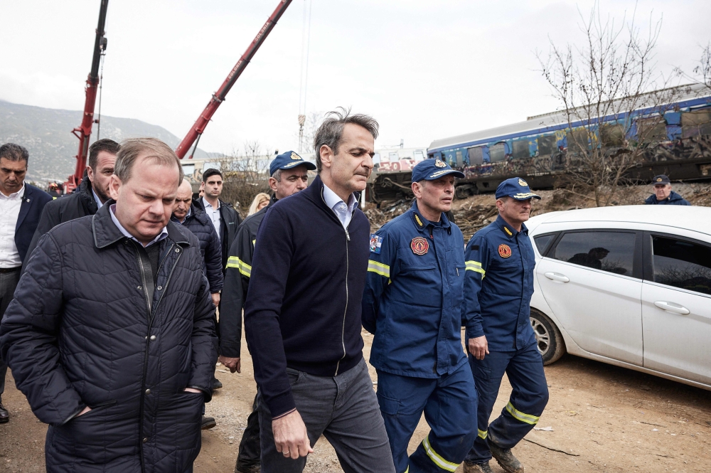 In this handout photograph taken on March 1, 2023 and released by the Greek Prime Minister's Office shows Greek transport minister, Kostas Karamanls (left) and Greek PM Kyriakos Mitsotakis (centre) visit the crash site following the deadly train accident where at least 38 people died and another 85 were injured near the Greek city of Larissa. Greece announced three days of national mourning. (Photo by Handout / AFP) 