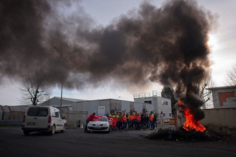 Unionists stand near a bonfire as they block access to the Storengy Site as they protest against the government's proposed pensions overhaul, which includes raising the minimum retirement age to 64 from 62 and increasing the number of years people have to make contributions for a full pension, in Chemery, central France, on March 17, 2023.  (Photo by GUILLAUME SOUVANT / AFP)
