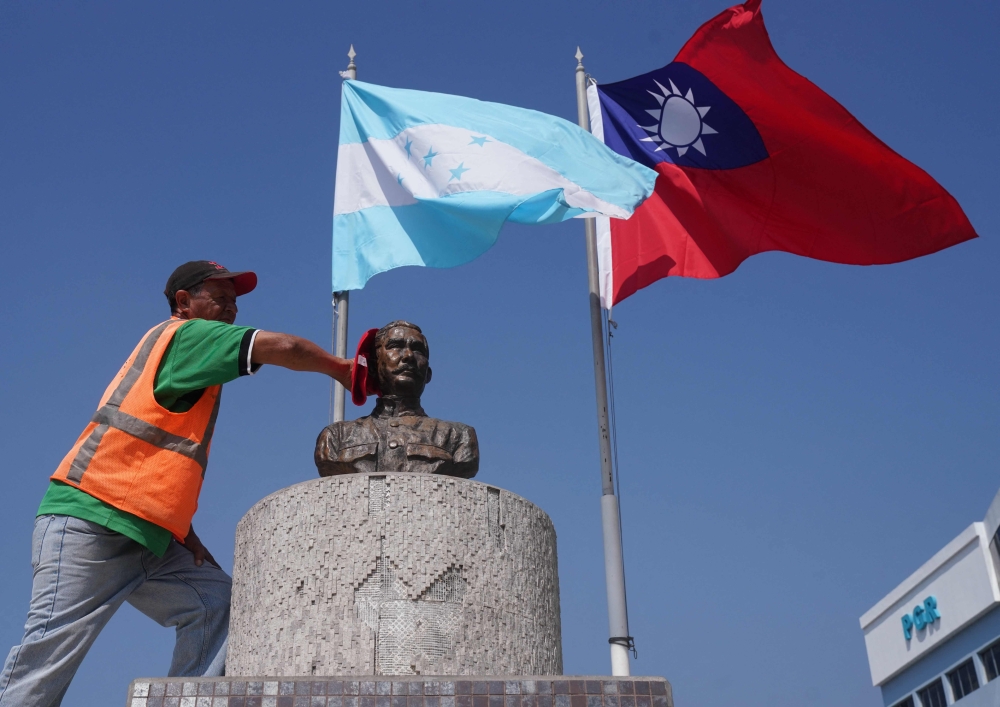 (FILES) In this file photo taken on March 15, 2023, a municipal worker cleans the bust of Sun Yat-sen, founder and first provisional president of the Republic of China, beneath the flags of Honduras (L) and Taiwan at a square in Tegucigalpa. (Photo by Stringer / AFP)