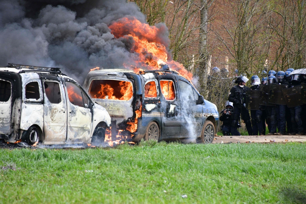 French gendarmes' stand next to gendarmes' cars burning on the sideline of a demonstration called by the collective 