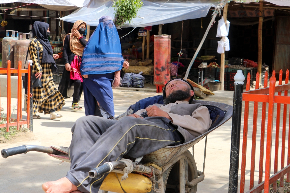 An Afghan daily worker sleeps on his wheelbarrow while women walk past at a market in Fayzabad district of Badakhshan province on April 10, 2023. (Photo by OMER ABRAR / AFP)