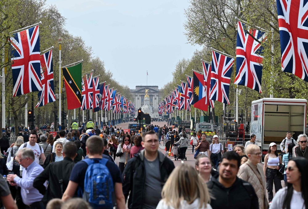 People walk beneath flags of the Union and Commonwealth along The Mall, towards Buckingham Palace, in central London, on April 30, 2023 ahead of the coronation ceremony of Charles III and his wife, Camilla, as King and Queen of the United Kingdom and Commonwealth Realm nations, on May 6, 2023. (Photo by JUSTIN TALLIS / AFP)