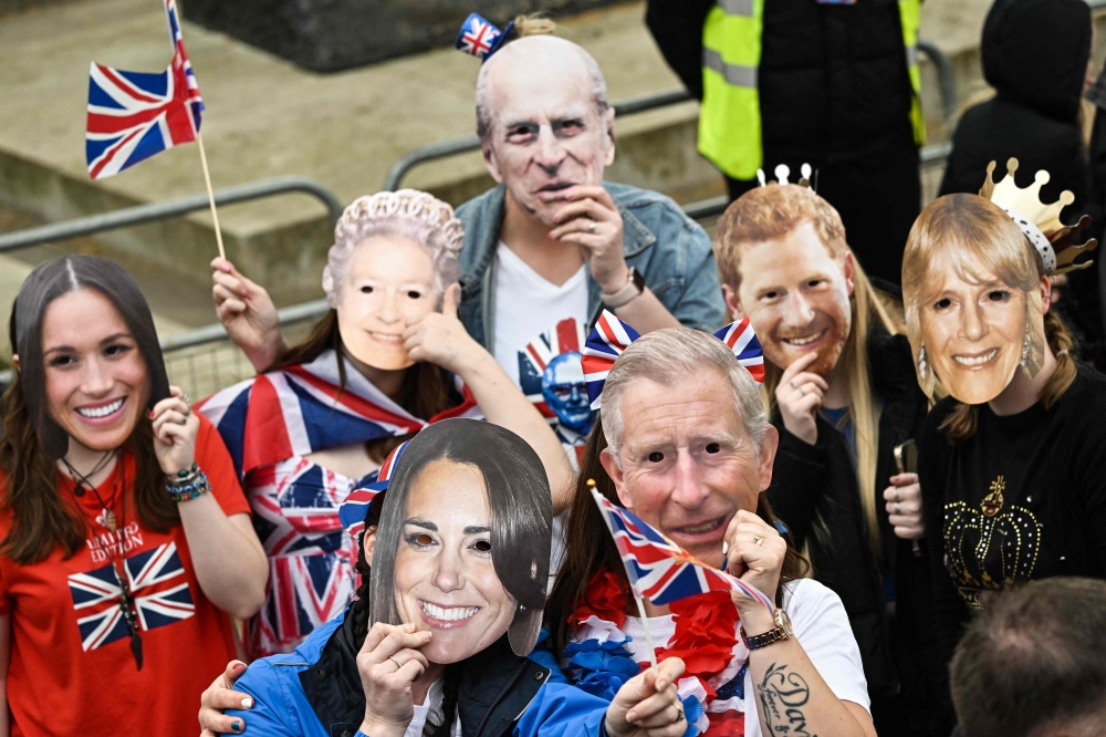 Well-wishers wearing masks of members of the Royal Family wait along the route of the 'King's Procession' (Photo by Loic Venance / AFP)