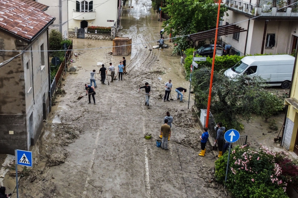 An aerial view taken on May 18, 2023 shows residents clearing mud in a street of Cesena after heavy rains caused flooding across Italy's northern Emilia Romagna region, killing five people. Photo by Alessandro SERRANO / AFP