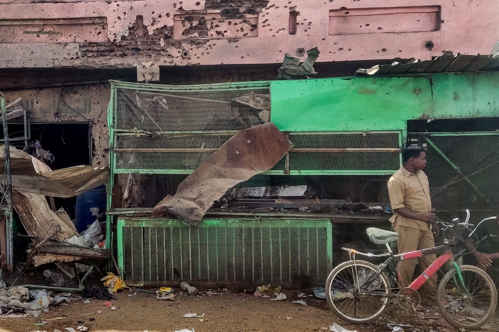A man stands with a bicycle by a medical centre building riddled with bullet holes at the Souk Sitta (Market Six) in the south of Khartoum on June 1, 2023. (Photo by AFP)