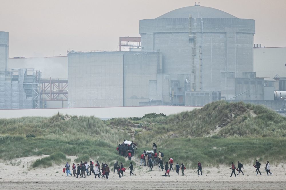 Migrants run up the dunes near Gravelines Nuclear Power Station to hide the smuggling boats from French National Police in Gravelines, northern France on June 12, 2023. (Photo by Sameer Al-Doumy / AFP)