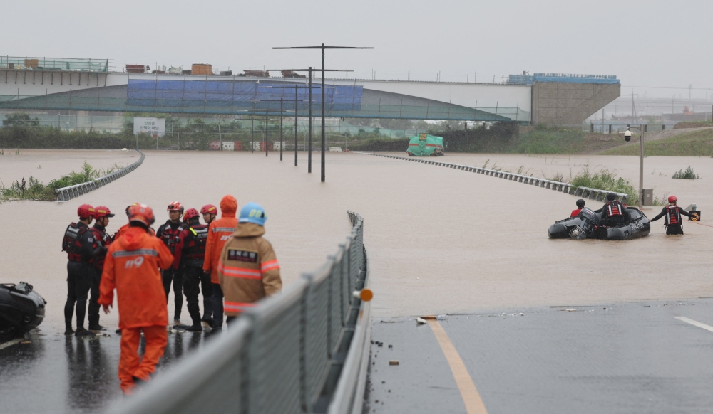 South Korean emergency workers search for survivors on a flooded road leading to an underground tunnel where some 19 cars were trapped by flood waters after heavy rains in Cheongju on July 15, 2023. (Photo by YONHAP / AFP)