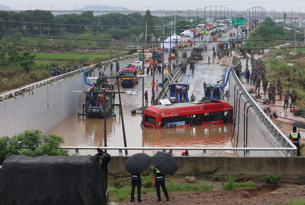 South Korean rescue workers search for missing persons near a bus along a deluged road leading to an underground tunnel where some 15 cars were trapped in flood waters after heavy rains in Cheongju on July 16, 2023. Photo by YONHAP / AFP)