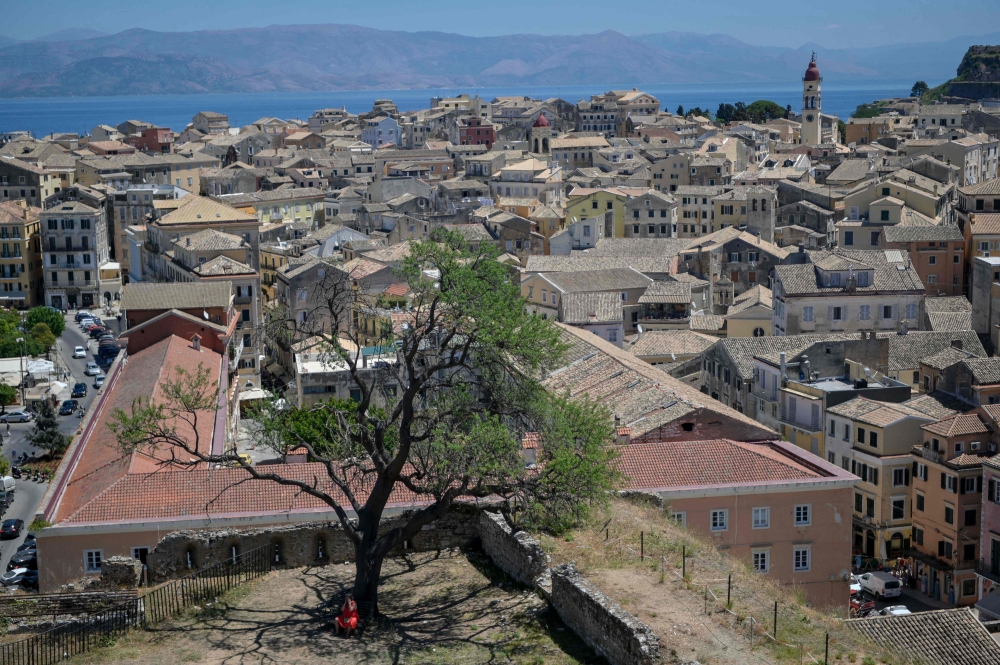 A woman sits under the shade of a tree overlooking the old town of the Greek Island of Corfu, during a heatwave, on July 28, 2023. (Photo by Armend NIMANI / AFP)