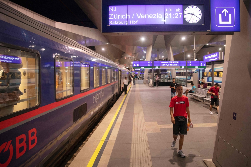 Passengers are seen on the platform in front of the Nightjet train line Vienna - Venice (-Zurich) of the Austrian Federal Railways (OeBB) as a sign shows the destinations and departure time at the main station in Vienna, Austria, on July 25, 2023. (Photo by Alex Halada / AFP)