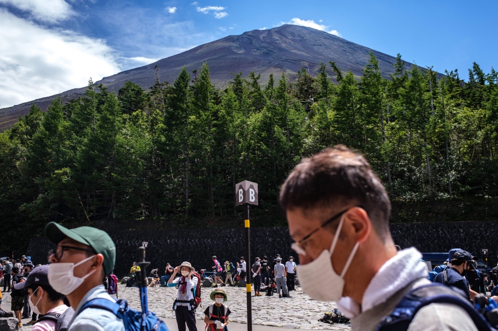 This picture taken on August 14, 2022 shows tourists gathered at the bus terminals of Fuji Subaru Line 5th Station with the background of Mount Fuji, Japan's highest mountain at 3,776 meters (12,388 feet). Photo by Philip FONG / AFP